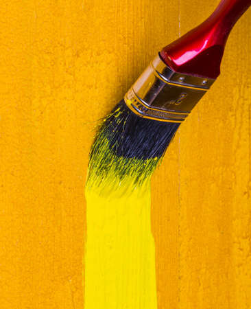 paintbrush with yellow paint dye a wooden wallの写真素材