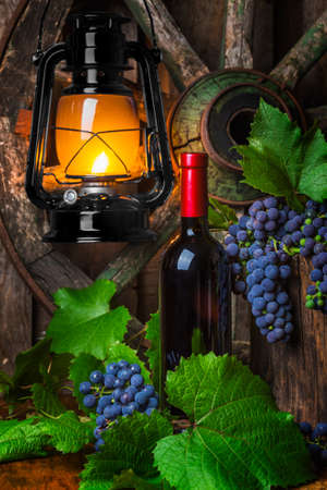Bottle of red wine with grapes on a background of a kerosene lampの写真素材