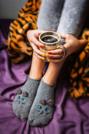 legs of girl in warm woolen socks and a cup of coffee warming, winter morning at homeの写真素材