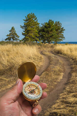 man holding a compass on the background of the road, field and treesの写真素材