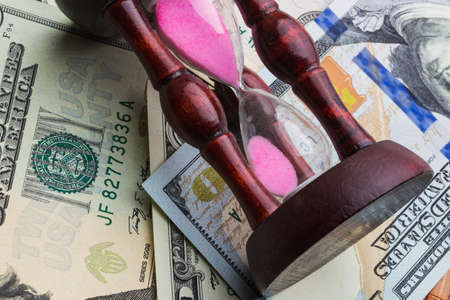 Time is money. An hourglass on the background of moneyの写真素材