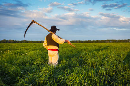 man in old clothes mows grass in the field