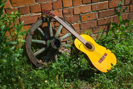Guitar and the old wagon wheel against a brick wallの写真素材