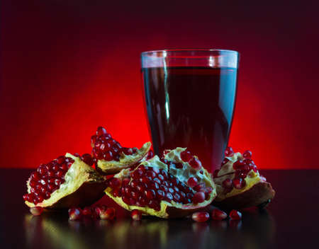 glass of pomegranate juice with pomegranate fruit in a dark  key on a red backgroundの写真素材