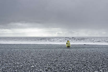 man in a yellow rain coat kneeling down at the oceanの写真素材