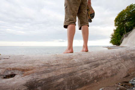 man standing barefoot man on a big driftwood tree trunk watching the ocean on the island of ruegen, germanyの写真素材