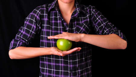 A girl holding a green apple with her two arms, on a black background  の写真素材