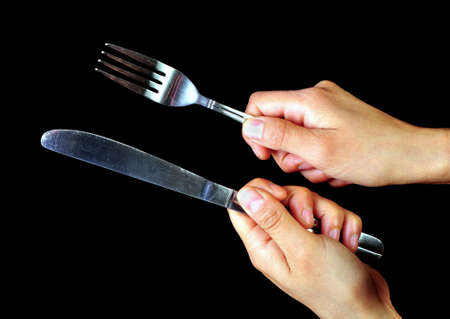 Pair of hands holding a fork and a knife on a black background  