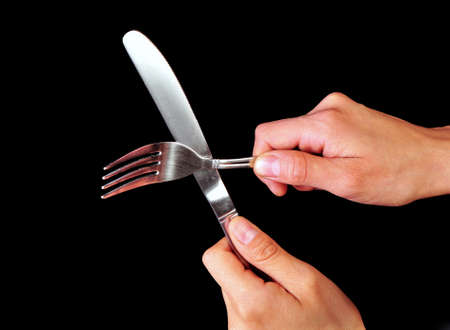Pair of hands holding a fork and a knife on a black background  