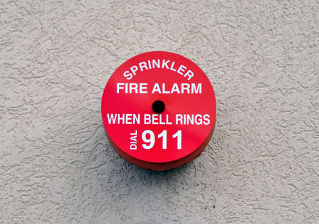 Red circular fire alarm on a beige colored wall   の写真素材