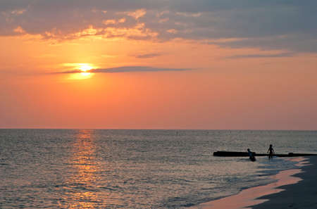 Children in silhouette playing in the water, late afternoon, close to sunset, at Madeira Beach, Florida, USA.の写真素材
