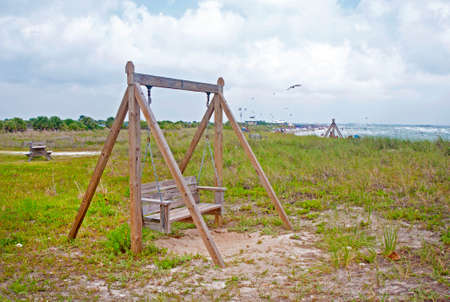 Wooden rocking bench, hanging with chains, at a local Florida beach on an overcast dayの写真素材