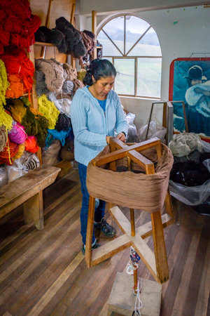 Guaranda, Bolivar province, Ecuador - November, 2013: Woman worker at a humble wool clothing shop, preparing wool on a wooden fabric holder, for sewing.のeditorial素材