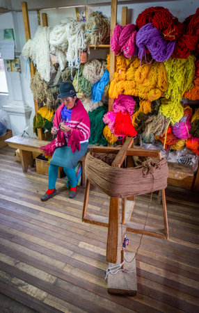 Guaranda, Bolivar province, Ecuador - November, 2013: A wooden fabric holder in the foreground, with wool, and a woman worker sewing in the background at, a humble wool clothing shop.のeditorial素材