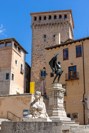 The statue of Juan Bravo stands before the Romanesque Church of San MartÃ­n in Segovia. The historic landmark, featuring a tall tower, is beautifully framed against a clear blue skyの写真素材