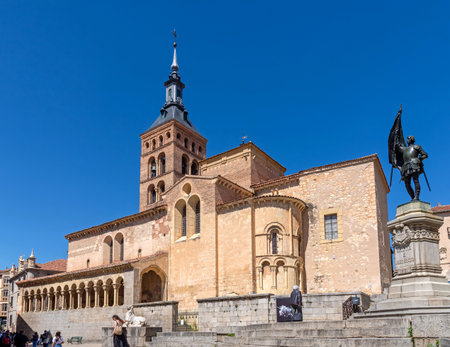 The statue of Juan Bravo stands before the Romanesque Church of San MartÃ­n in Segovia. The historic landmark, featuring a tall tower, is beautifully framed against a clear blue skyの写真素材