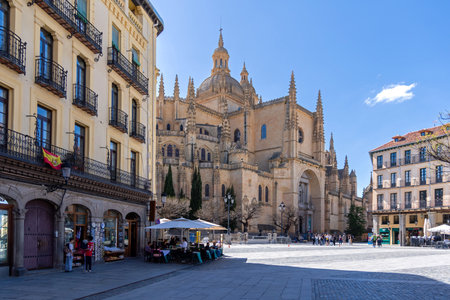 Segovia's massive Cathedral of Santa MarÃ­a dominates the plaza. Its Gothic style towers over the bustling public space, where Segovian life unfolds under a blue skyの写真素材
