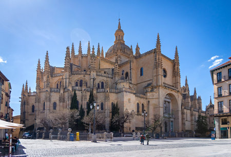 Segovia's massive Cathedral of Santa MarÃ­a dominates the plaza. Its Gothic style towers over the bustling public space, where Segovian life unfolds under a blue skyの写真素材