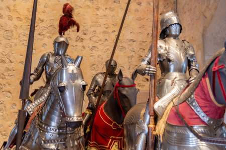 Medieval suits of armor inside Segovia's AlcÃ¡zar reflect light. Steel breastplates and helmets stand by a wall-mounted heraldic shieldの写真素材