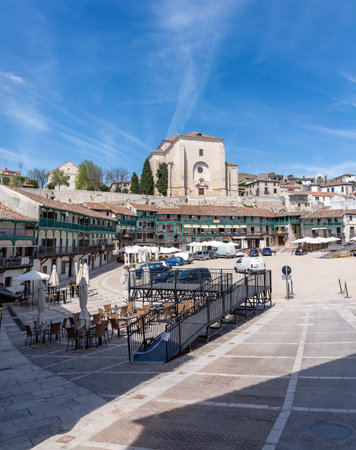 The unique, irregular Plaza Mayor of ChinchÃ³n, Spain, featuring three stories of wooden balconied buildings and the Church of Our Lady of the Assumption in the backgrounの写真素材