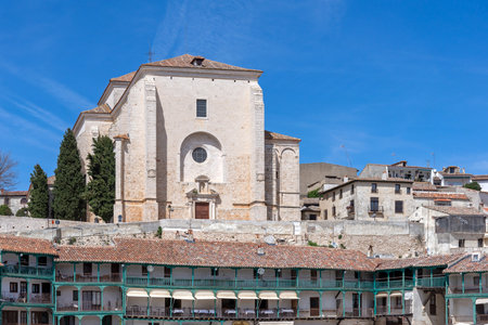 The unique, irregular Plaza Mayor of ChinchÃ³n, Spain, featuring three stories of wooden balconied buildings and the Church of Our Lady of the Assumption in the backgrounの写真素材