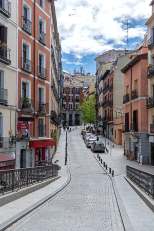 Tall, traditional brick and plaster buildings line the old paved streets of central Madrid, featuring multiple stories and rows of ornate, wrought-iron balconiesの写真素材