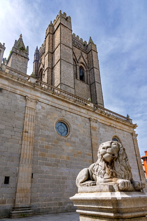 A low-angle view of the Gothic tower of Ãvila Cathedral, with a carved stone lion on a pedestal in the foreground set against the cathedralâs massive stone wallsの写真素材