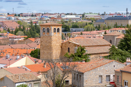 Panoramic view over Ãvilaâs terracotta rooftops, centered on a square golden-brown Romanesque church tower, with the modern city reaching toward the cloudy horizonのeditorial素材