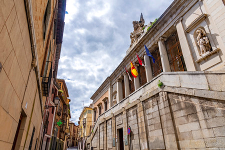 Wide-angle view of the old Palacio Universitario in Toledo with its grand stone stairs, classical columns, and statues under a cloudy sky. Narrow street on the leftのeditorial素材