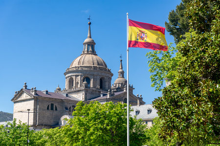 A Spanish flag flies before the grand dome and granite walls of El Escorial monastery in San...