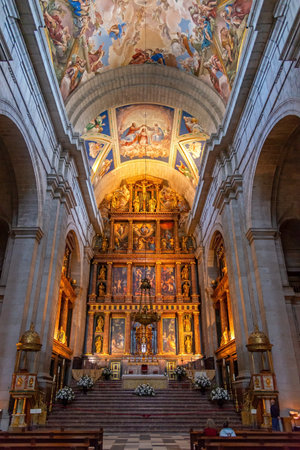 The grand gilded altar and frescoed vaulted ceiling of the Basilica of San Lorenzo de El Escorial in Spain, featuring intricate religious art and golden statuesのeditorial素材