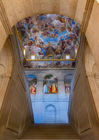 The grand Great Staircase of El Escorial in Spain features massive granite arches leading to a...