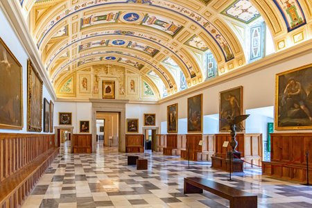 The Gallery of Paintings at El Escorial in Spain features a long hall with an ornate vaulted...