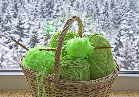 Green skeins and crochet hooks are in the basket on background snowy forestの写真素材