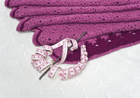 Pink knitwear, centimeter and a crochet hook are on the background of white openwork knitted fabricの写真素材