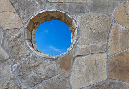 Wall of rough stone with a round hole through which one can see the skyの写真素材