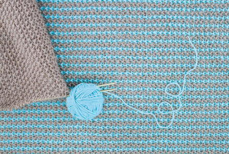 Brown knitwear with knitting needles are on the background of turquoise knitwear