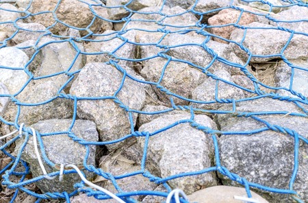 Gabion-grey stones kepted with lattice made of blue wire.Closeup. Small depth of field.の写真素材