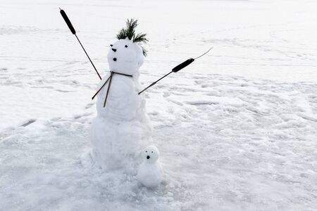 Family snowmen of two figures with hands up on background of snowの写真素材