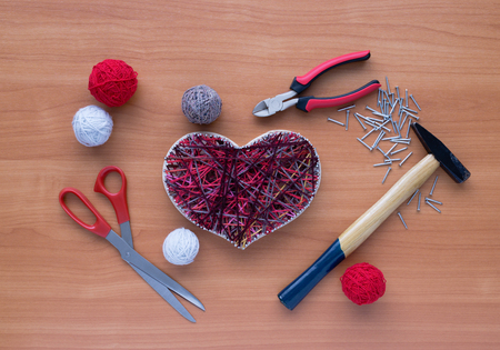 Panel of heart shaped of thread and nails, hammer, scissors, nippers and clews are on wooden tableの写真素材