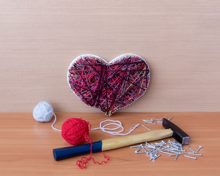 Panel of heart shaped of thread and nails, hammer and clews are on wooden table with copy spaceの写真素材
