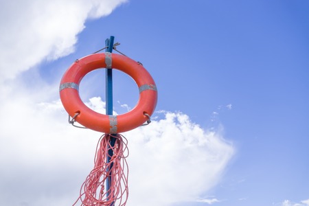 Orange lifebuoy with ropes against background cloudy skyの写真素材