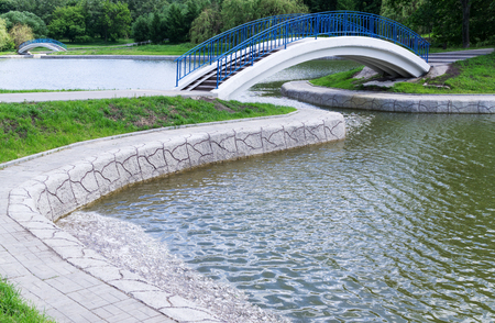 Pedestrian arch bridge with blue railing above pond is in parkの写真素材