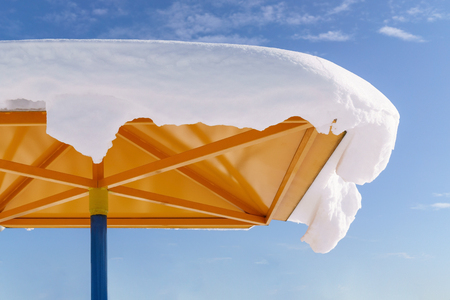 Roof of yellow sunshade covered snow against background of blue sky.の写真素材