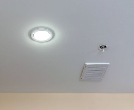 Round lamp with turned on bulb, ventilation hatchway and sensor of fire safety are on suspended ceiling. Copy spaceの写真素材