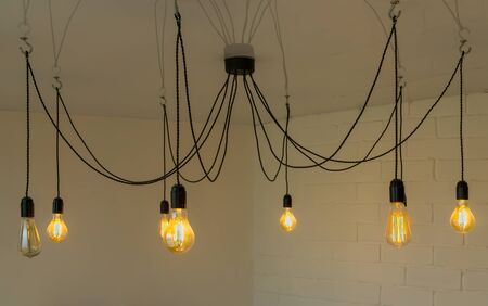 Burning electric light bulbs hanging on wires are on brick wall background. Small depth of fieldの写真素材