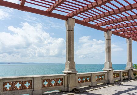 Pergola with stone pillars and fence is on promenade of resort against  backdrop of sea landscape. Sunny dayの写真素材
