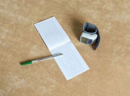 Wrist blood pressure monitor and diary of observations lying on couch. View from topの写真素材
