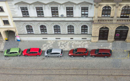 Autos parked on street is cobblestone near old building. View from topの写真素材