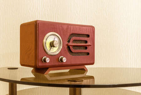 Wooden retro radio receiver is on glass coffee table near wall. Copy space